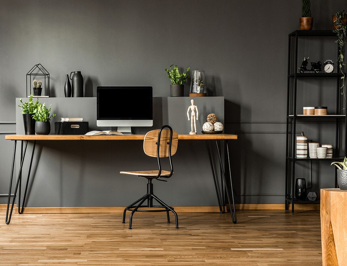 Stilvolles Home-Office mit einem minimalistischen Schreibtisch aus Holz, grauer Wandfarbe und modernen Dekorationsartikeln.
