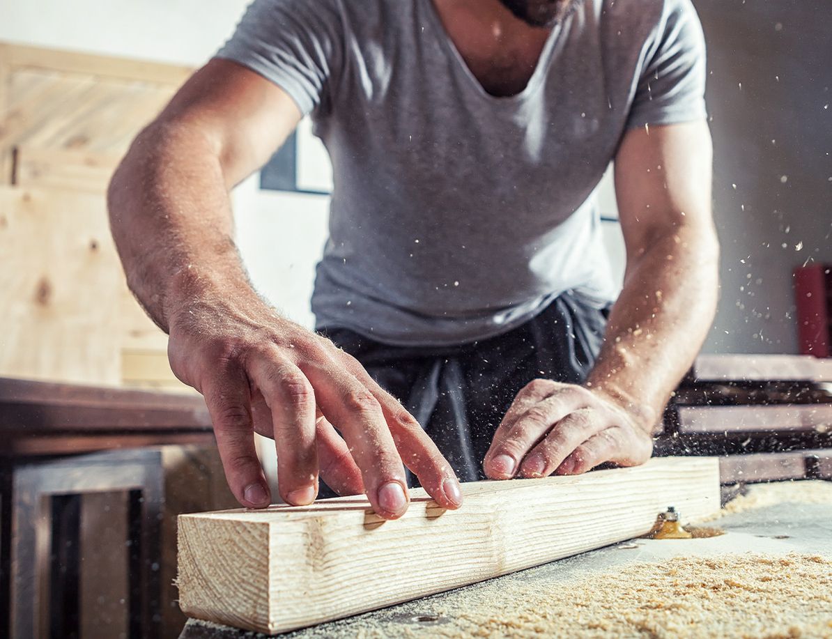 Handwerker bearbeitet ein Holzstück auf einer Hobelbank, Sägemehl fliegt in die Luft.
